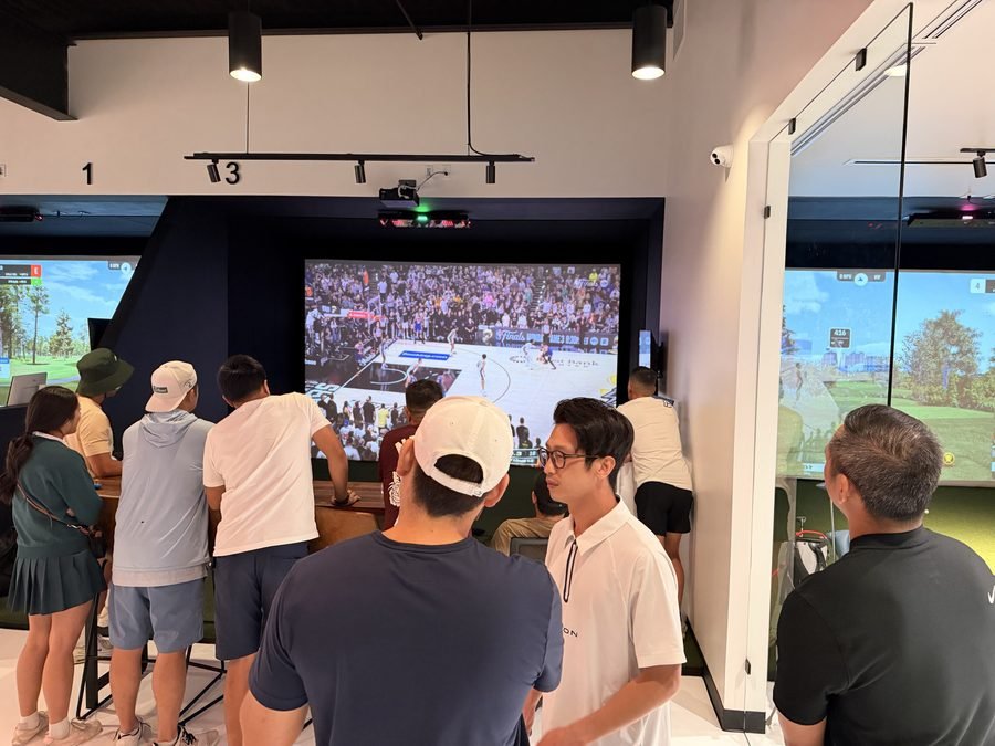 A crowd at Birdie Central watching a game on the big screen between the simulator bays